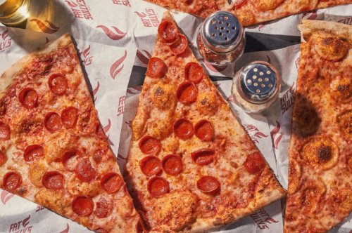 Close-up of pizza slices topped with pepperoni, surrounded by salt and pepper shakers on branded paper.