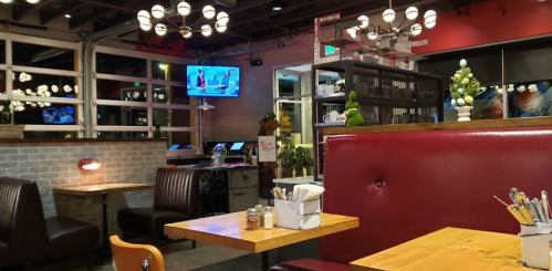 Cozy restaurant interior with wooden tables, red booths, and a TV, featuring plants and modern lighting.