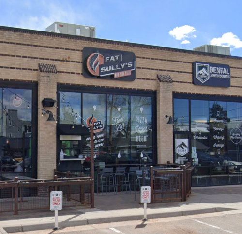 Exterior of Fat Sully's restaurant with large windows, outdoor seating, and a dental office sign nearby.