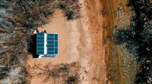 Aerial view of a small building with solar panels near a riverbank surrounded by bare trees and dry land.