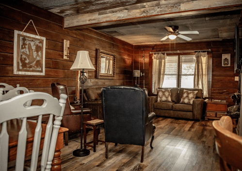 Cozy living room with wooden walls, a ceiling fan, comfortable seating, and a warm, inviting atmosphere.