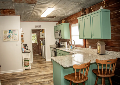 Bright kitchen with teal cabinets, granite countertops, and wooden accents, featuring a doorway leading to another room.