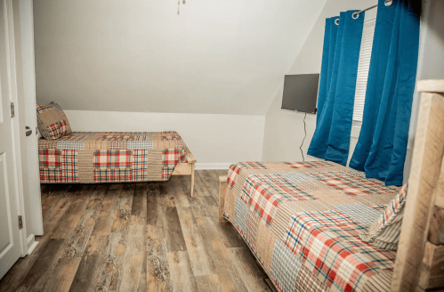 A cozy room with two twin beds, plaid bedding, blue curtains, and a wall-mounted TV.