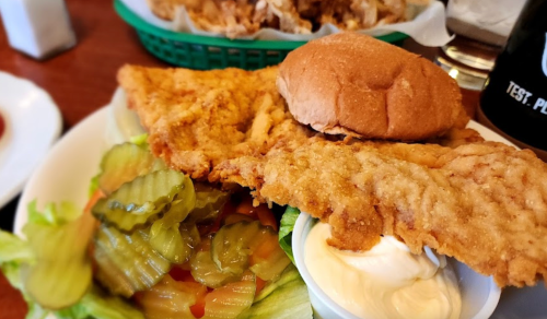 A plate featuring a fried chicken sandwich with pickles, lettuce, and a side of mayonnaise.