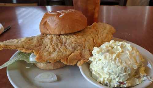 A large fried fish fillet on a bun with lettuce, served alongside a scoop of potato salad.