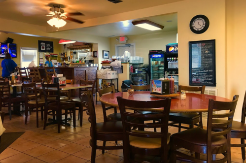 A cozy restaurant interior with wooden tables, chairs, a bar area, and a chalkboard menu on the wall.