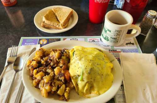 A plate of eggs Benedict with hash browns, toast, a coffee mug, and a red drink on a diner table.