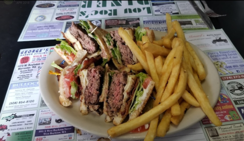 A plate of stacked sandwiches with lettuce and tomato, accompanied by a side of golden French fries.