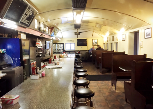 A retro diner interior with a long counter, stools, and wooden booths, featuring vintage decor and a cozy atmosphere.