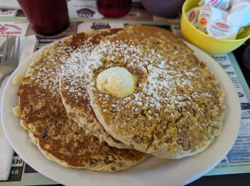 Three large, golden-brown pancakes topped with a pat of butter and powdered sugar, served on a white plate.