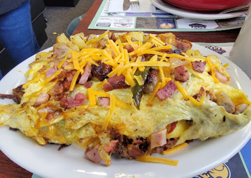 A hearty breakfast plate featuring an omelette topped with cheese, ham, sausage, and crispy potatoes.