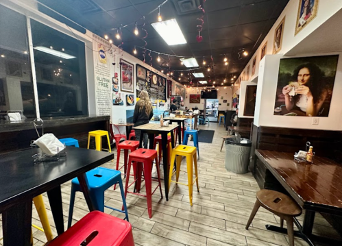 A cozy restaurant interior with colorful stools, artwork on the walls, and a customer at a table.