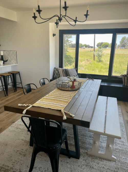 A modern dining area featuring a wooden table, black chairs, a striped table runner, and a large window with a view.