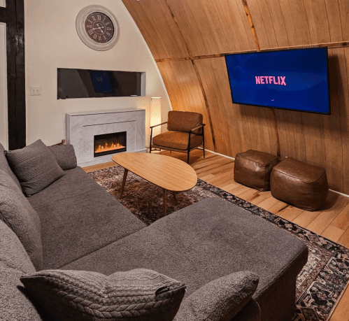 Cozy living room with a gray sofa, coffee table, and a TV displaying Netflix, featuring a faux fireplace and warm decor.