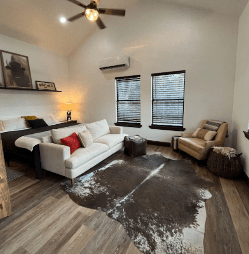 Cozy living space featuring a sofa, armchair, and a cowhide rug, with large windows and modern decor.