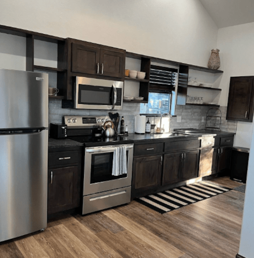 Modern kitchen with dark wood cabinets, stainless steel appliances, and a striped rug on a wooden floor. Bright and spacious.