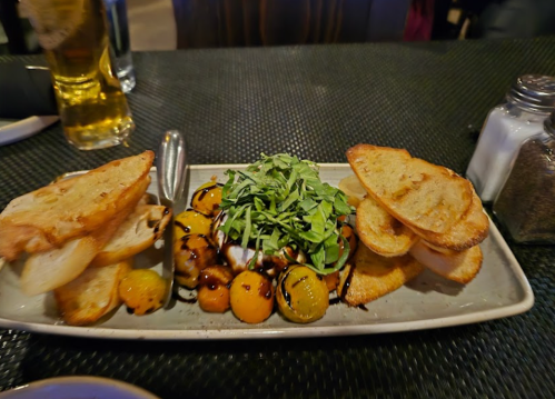 A plate of toasted bread with a salad of mixed greens and colorful tomatoes drizzled with balsamic glaze.