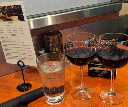 Two glasses of red wine and a glass of water on a wooden table, with a menu and a candle in the background.