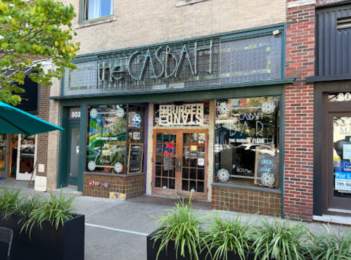 Exterior of The Casbah, a restaurant with large windows and a decorative sign, surrounded by greenery and urban architecture.