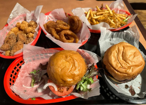 A tray with two burgers, onion rings, chicken bites, and fries, all served in red baskets lined with paper.