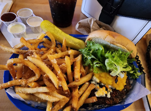 A plate of crispy fries, a burger with lettuce and pickles, and a drink, all on a wooden table.
