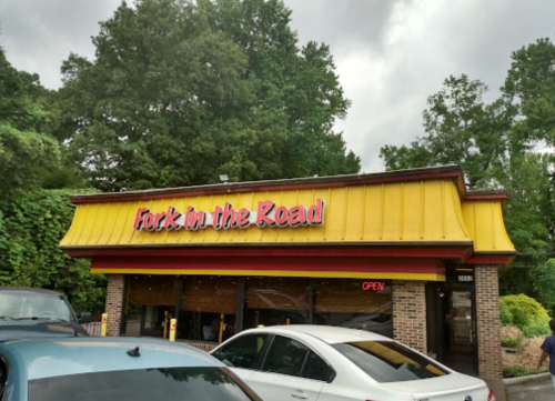 A restaurant named "Fork in the Road" with a yellow roof and an "OPEN" sign, surrounded by trees and parked cars.