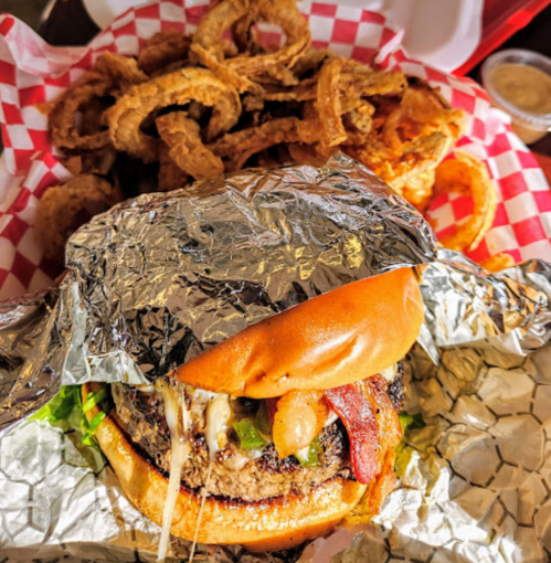 A juicy burger with melted cheese, lettuce, and bacon, served with a side of crispy onion rings in a checkered basket.