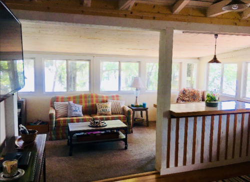 Cozy living area with large windows, a sofa, coffee table, and a view of nature outside. Warm, inviting atmosphere.