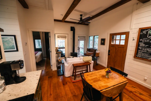Cozy interior of a cabin with wooden beams, a dining table, and a living area featuring a sofa and large windows.