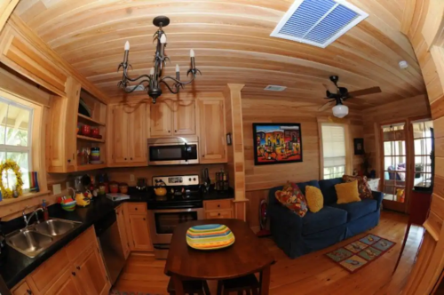 Cozy wooden kitchen and living area with a table, couch, and modern appliances, featuring warm lighting and decor.