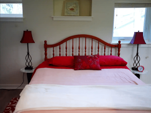 Cozy bedroom with a red and pink bedspread, decorative pillows, and matching lamps on bedside tables.