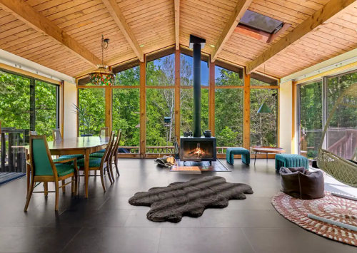 Bright, modern living space with large windows, wooden beams, a fireplace, and a cozy dining area.