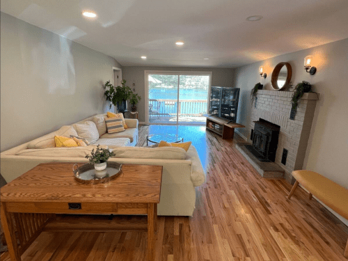 Cozy living room with a large sofa, wooden table, and a view of the water through sliding glass doors.