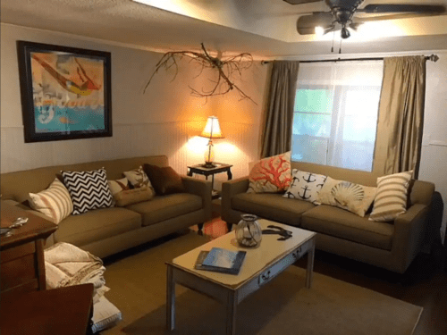 Cozy living room with two sofas, decorative pillows, a lamp, and a coffee table, featuring nautical-themed decor.