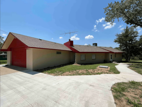 A single-story house with a red roof and garage, surrounded by grass under a clear blue sky.