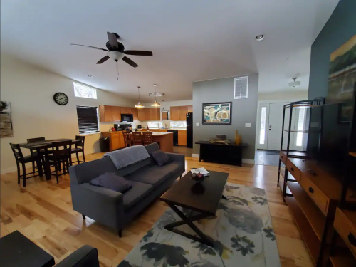 A spacious living room with a gray sofa, coffee table, and dining area, featuring wooden floors and modern decor.