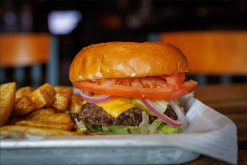 A close-up of a juicy cheeseburger with lettuce, tomato, and onion, served with golden fries on the side.