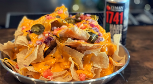 A plate of nachos topped with melted cheese, jalapeños, and diced onions, alongside a can of hard seltzer.