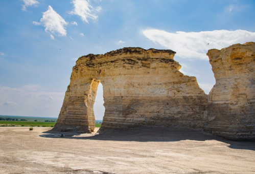 A large rock formation with a natural arch, set against a blue sky and open landscape.
