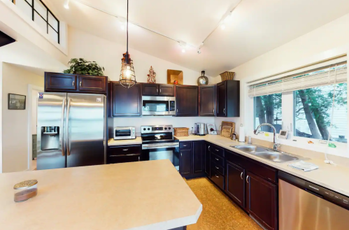 Modern kitchen with dark wood cabinets, stainless steel appliances, and a large window overlooking greenery.