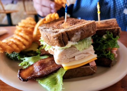 A hearty sandwich with turkey, cheese, lettuce, and bacon, served with crinkle-cut fries on the side.