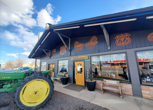 A Route 66-themed store with a yellow door, surrounded by vintage signs and a green tractor in front.