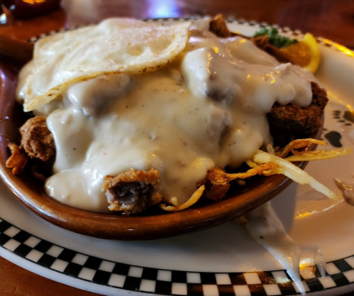 A bowl of crispy fried food topped with creamy gravy and a fried egg, served with a slice of orange.