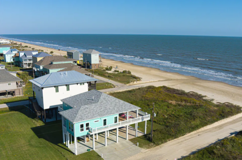 Aerial view of beach houses along a sandy shore with ocean waves and clear blue skies.