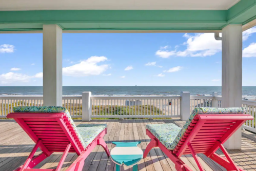 Two colorful lounge chairs on a deck overlooking a beach and ocean under a clear blue sky.