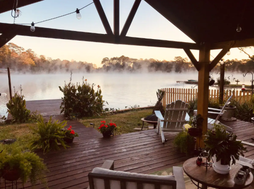 A serene lakeside view at dawn, featuring mist over the water and cozy seating under a wooden gazebo.