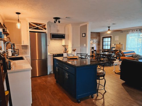 A modern kitchen with dark blue island, stainless steel appliances, and an open living area with cozy seating.