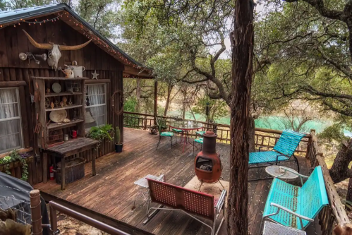 Cozy wooden deck surrounded by trees, featuring seating areas and a rustic cabin in a serene outdoor setting.