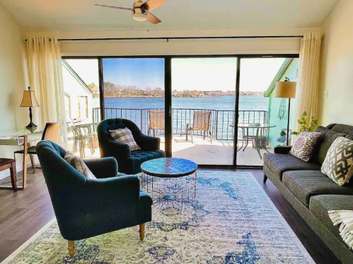 Cozy living room with two chairs, a coffee table, and a view of a lake through large sliding glass doors.