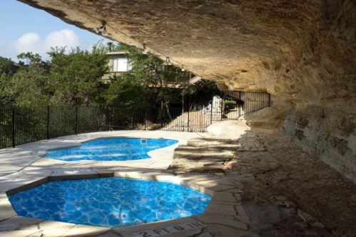 Two blue hot tubs nestled against a rocky cliff, surrounded by greenery and a black fence.